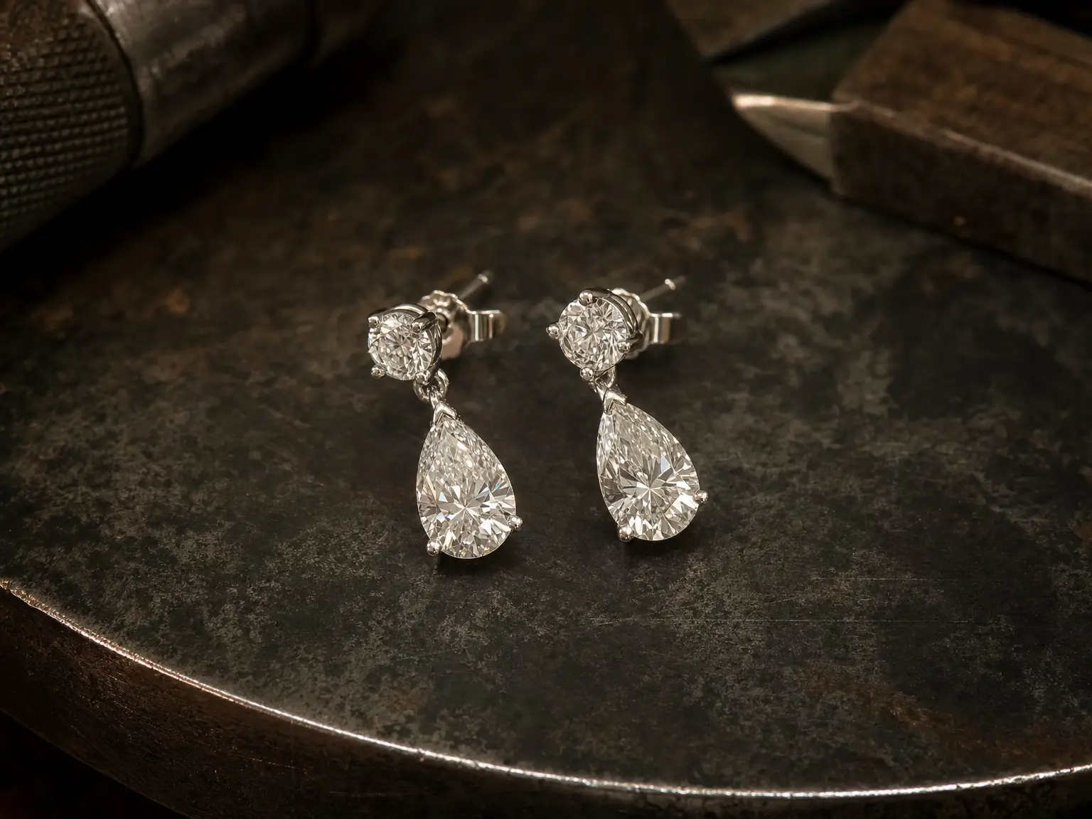 A pair of white gold pear-shaped natural diamond drop earrings on a jeweller's bench