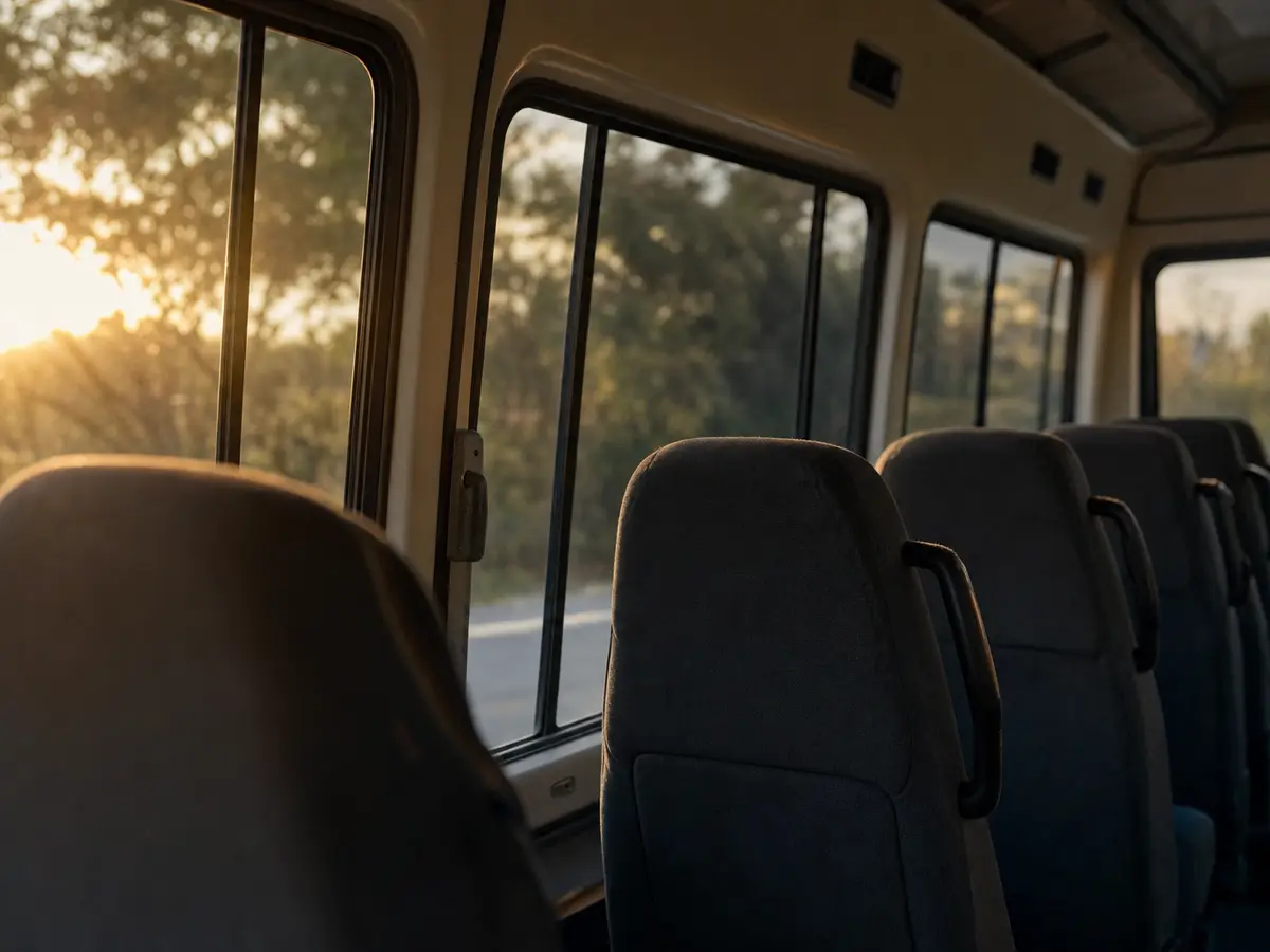 A row of empty seats inside a small bus, lit by evening light through the windows