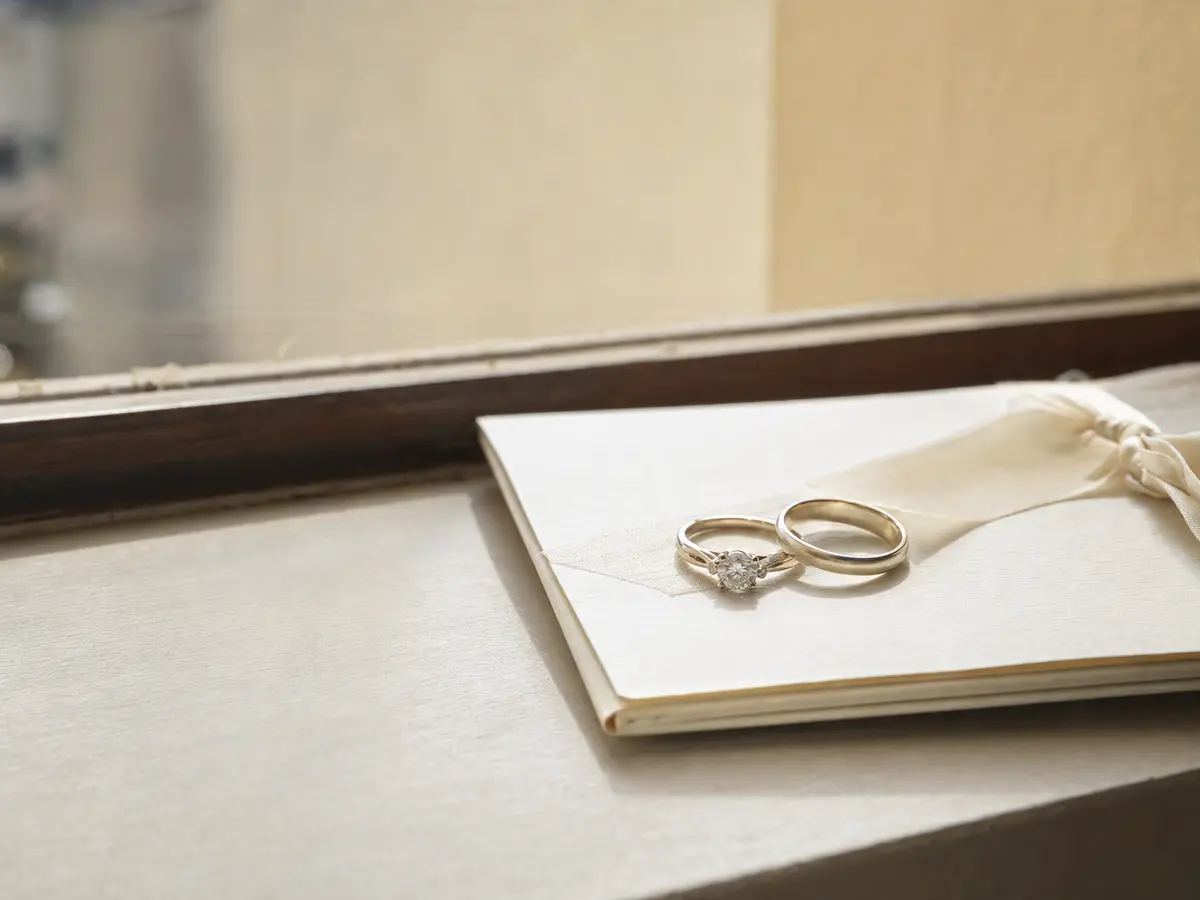 A wedding band and an engagement ring on a folded order of service, morning light through a window
