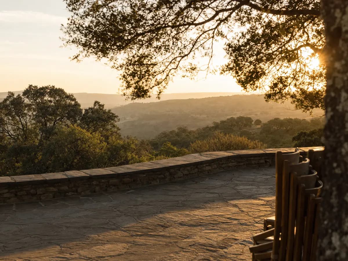 An empty stone terrace above a valley in the late afternoon, chairs stacked to one side and the light going gold