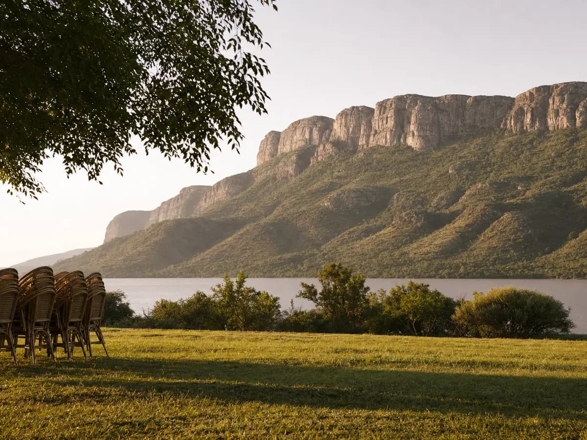 An open lawn above Hartbeespoort Dam at last light, the Magaliesberg escarpment behind it, chairs not yet set out