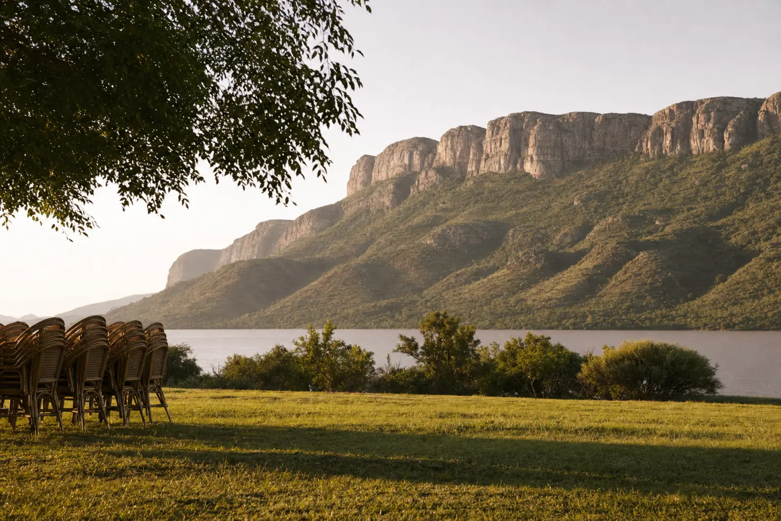 An open lawn above Hartbeespoort Dam at last light, the Magaliesberg escarpment behind it, chairs not yet set out