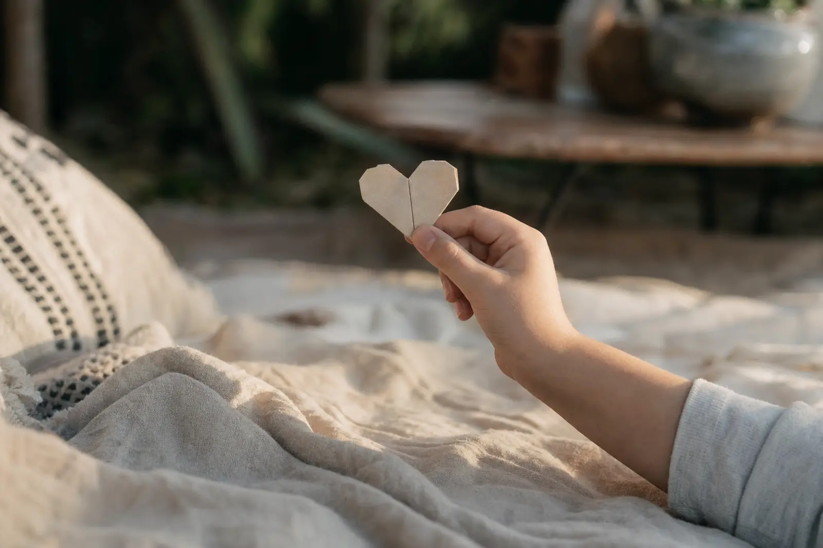 A child's small hand holding a folded paper heart on a picnic blanket