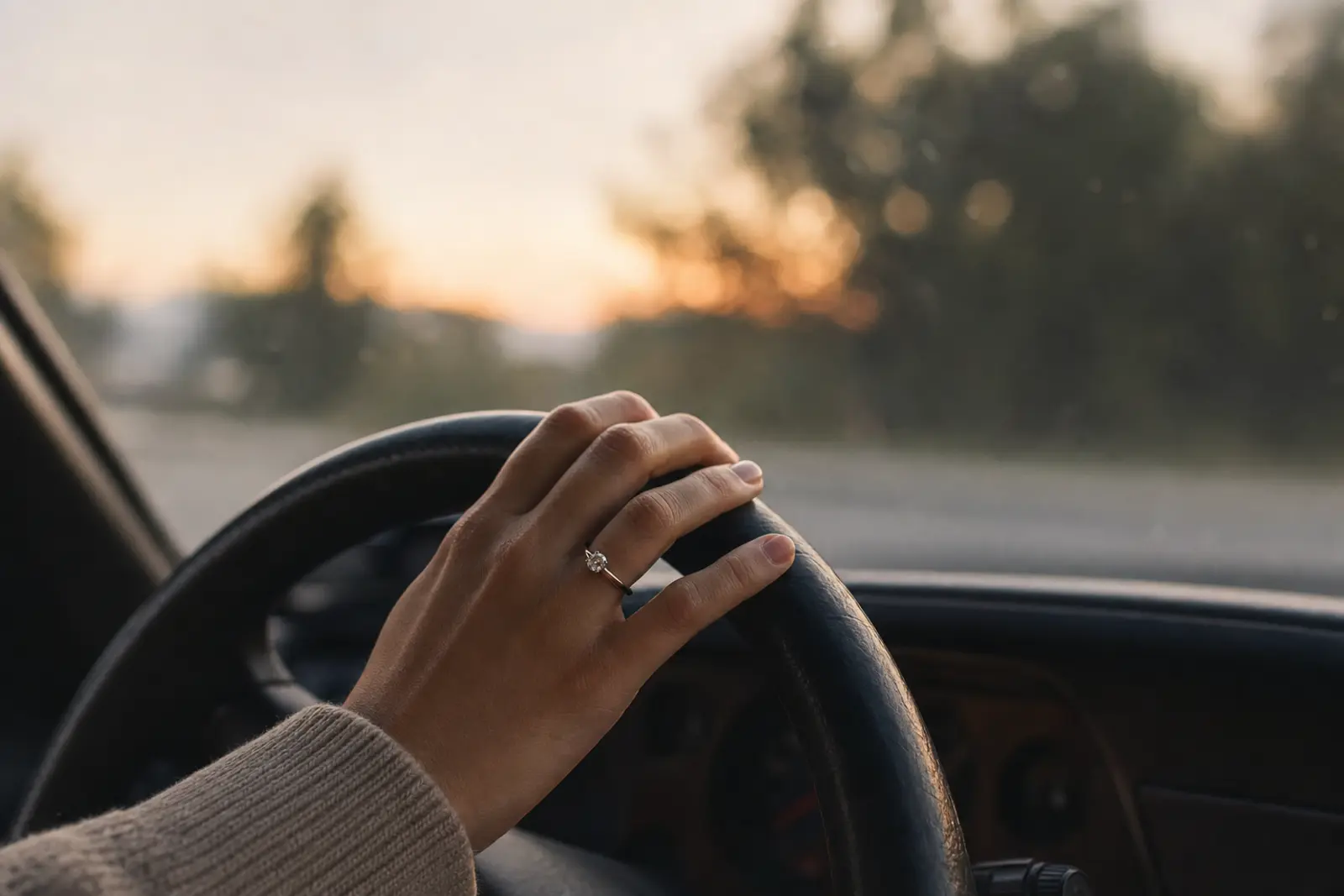 A hand wearing a new ring resting on a car steering wheel at dusk