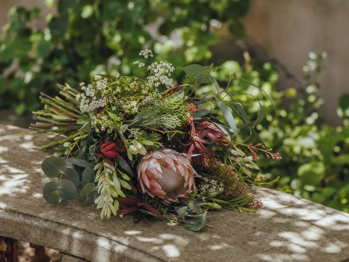 A single small arrangement of seasonal flowers set on a stone bench in dappled shade