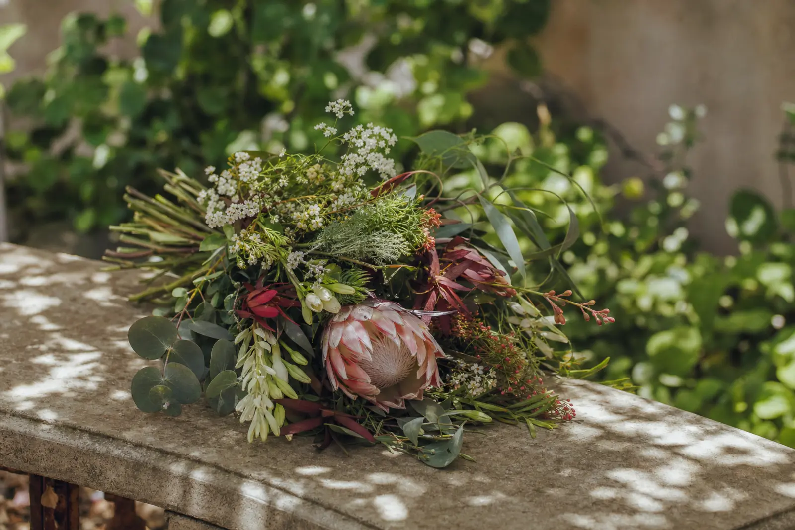 A single small arrangement of seasonal flowers set on a stone bench in dappled shade