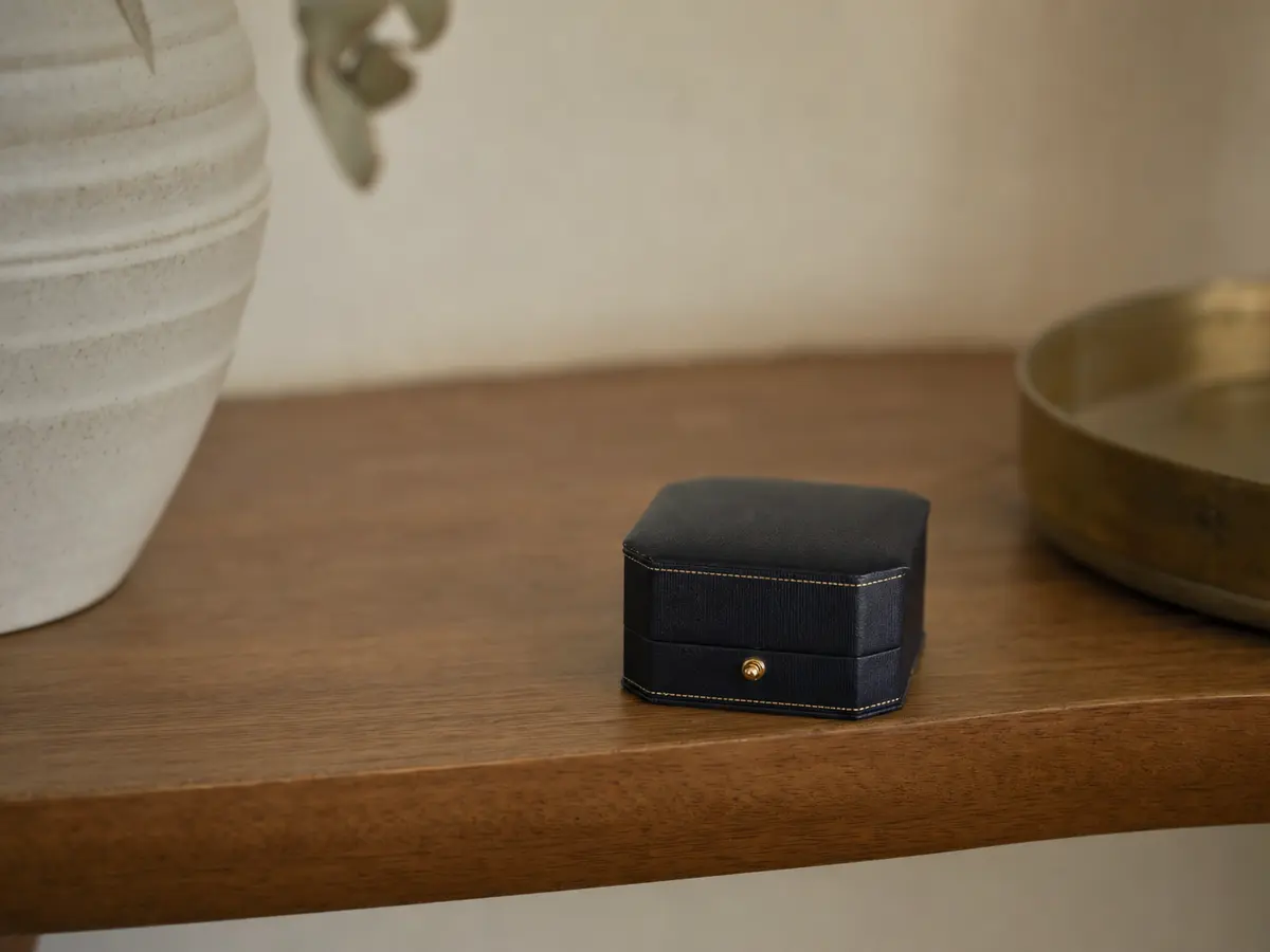 A closed ring box set aside on a shelf, slightly out of focus, with nothing else on the shelf