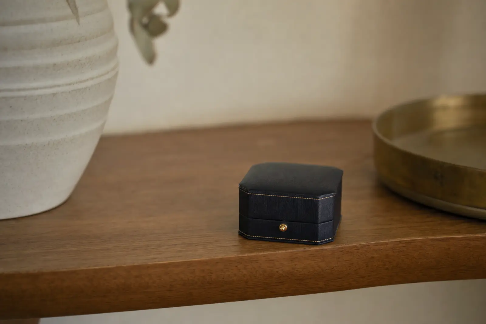 A closed ring box set aside on a shelf, slightly out of focus, with nothing else on the shelf
