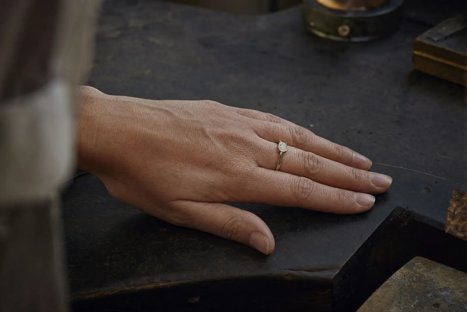 A hand at rest on a dark bench wearing a ring sized and scaled to it, seen from above