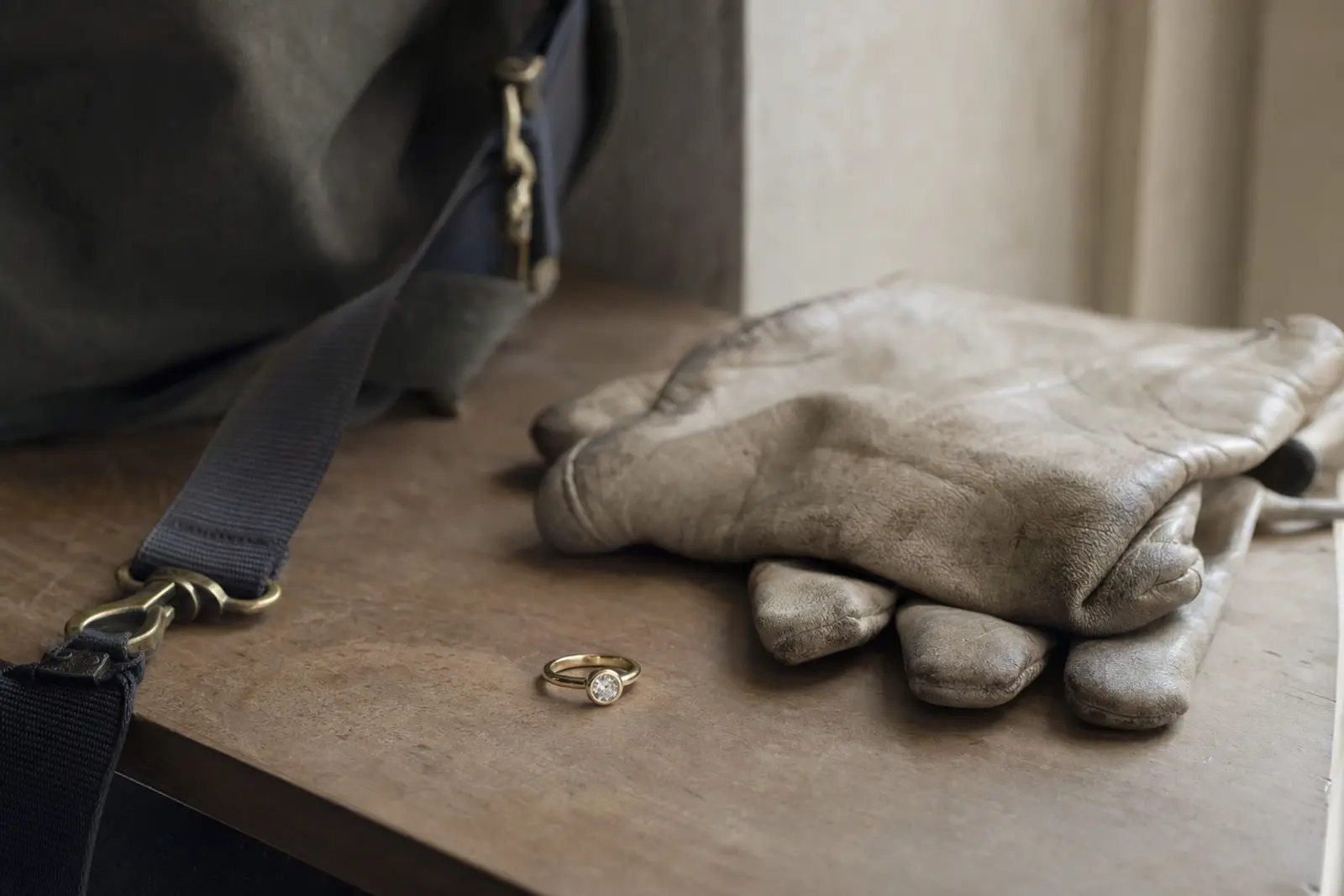A plain low-set engagement ring beside a pair of work gloves and a gym bag on a bench