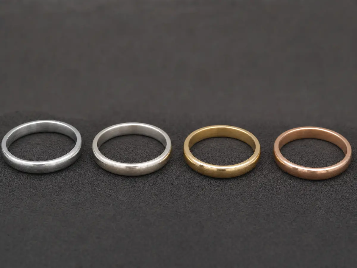 Four unset ring bands in platinum, white gold, yellow gold and rose gold laid in a row on dark suede