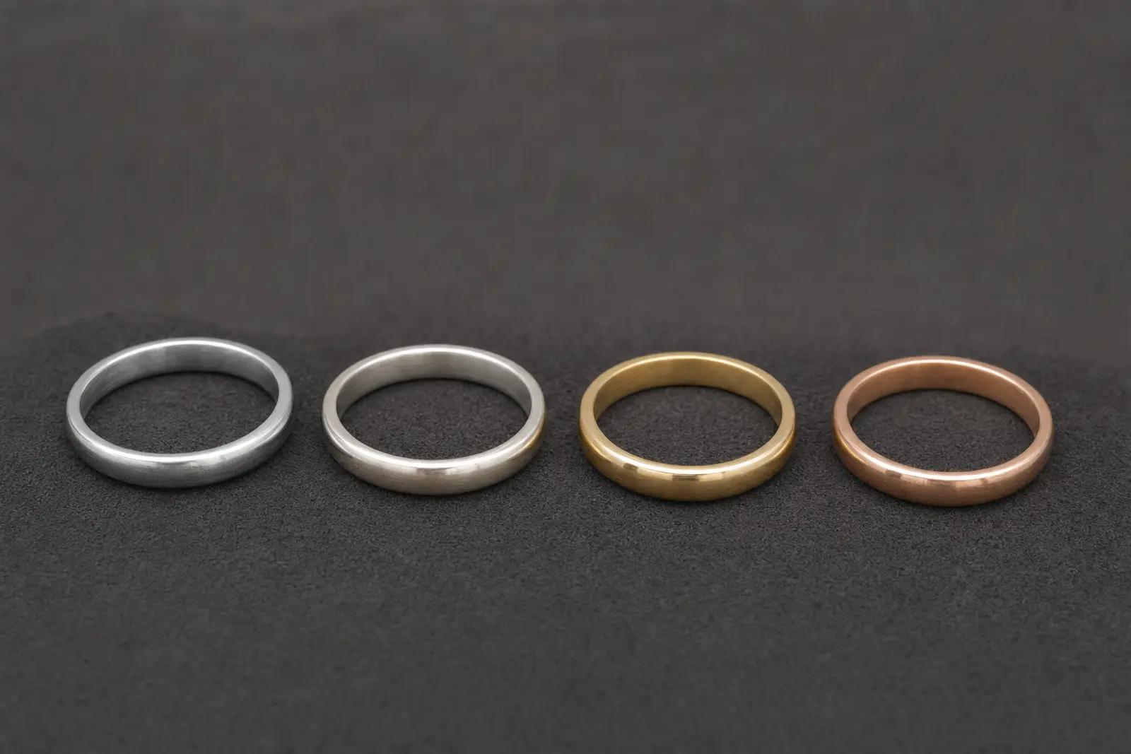 Four unset ring bands in platinum, white gold, yellow gold and rose gold laid in a row on dark suede