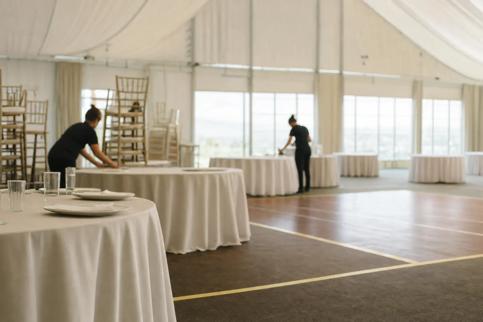 An empty function room mid-set-up, with round tables half-dressed and a bare dance floor marked out with tape