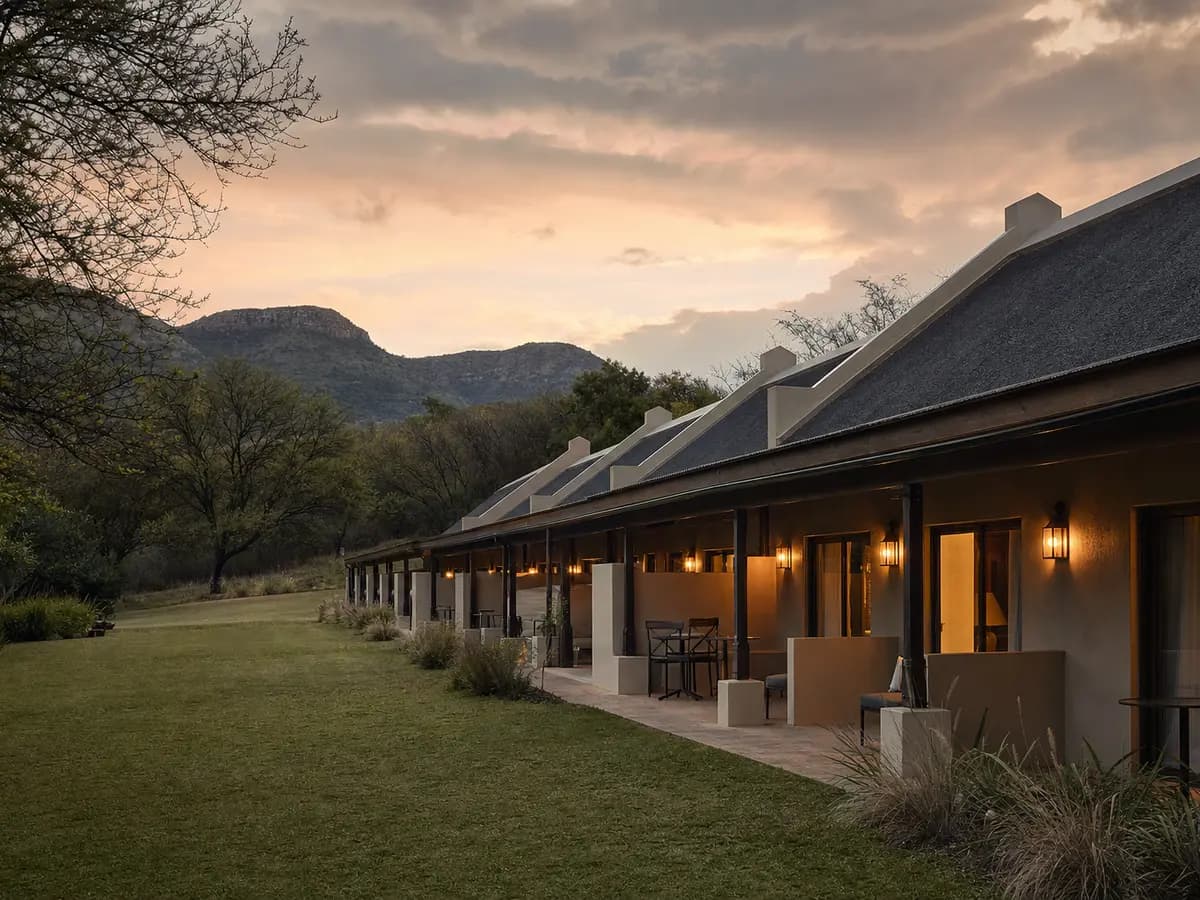 A lodge-style accommodation wing beside a wedding venue's lawn in the Magaliesberg region at dusk