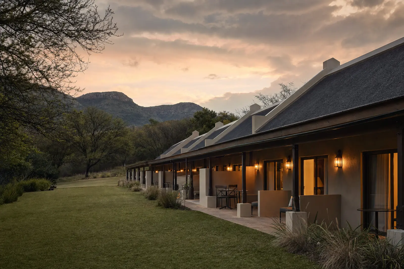 A lodge-style accommodation wing beside a wedding venue's lawn in the Magaliesberg region at dusk