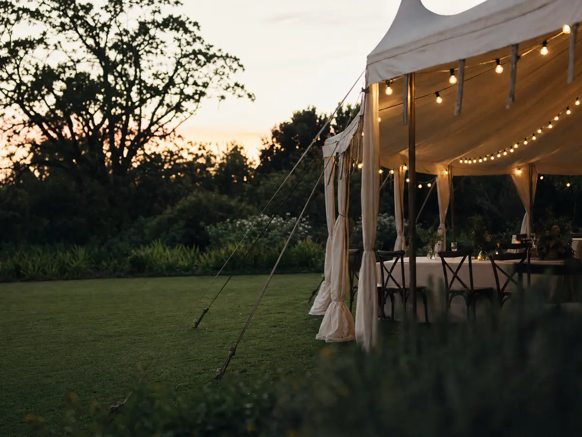 A garden marquee edge with string lighting at dusk, lawn and trees beyond, no people