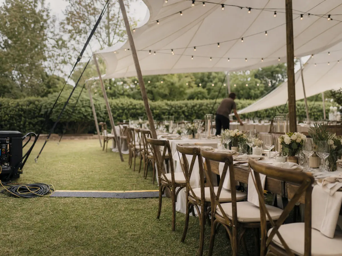 A marquee being set up on a suburban lawn with long tables and string lighting overhead