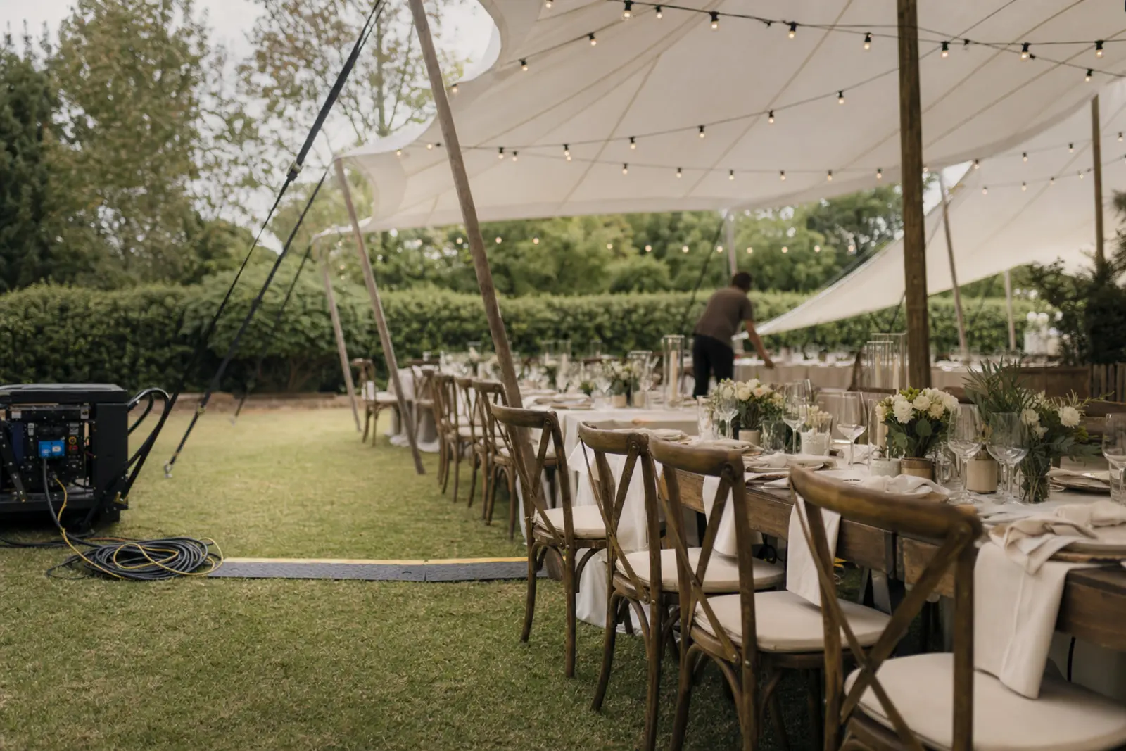 A marquee being set up on a suburban lawn with long tables and string lighting overhead