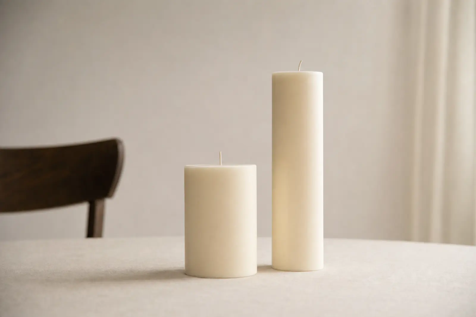 Two unlit candles of different heights standing side by side on a plain table