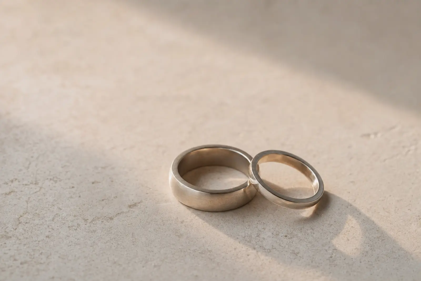 Two wedding bands of different widths resting together on a pale stone surface in soft afternoon light