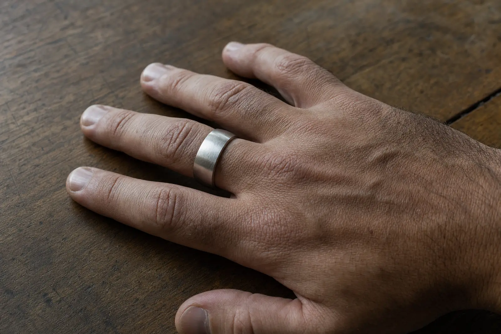 A wide brushed platinum band on a man's hand resting on a workbench