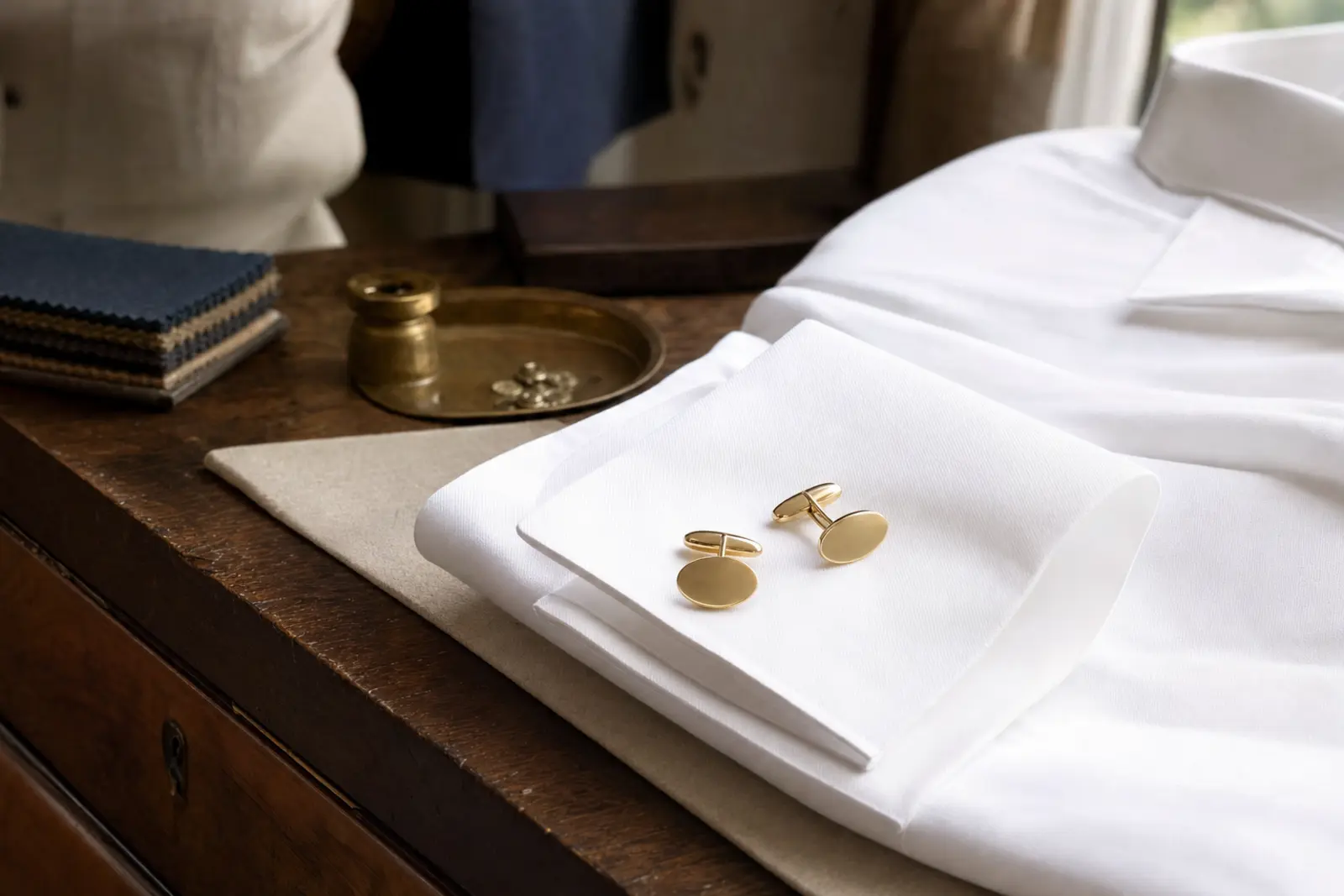 A pair of oval gold cufflinks resting on a folded white French-cuff shirt