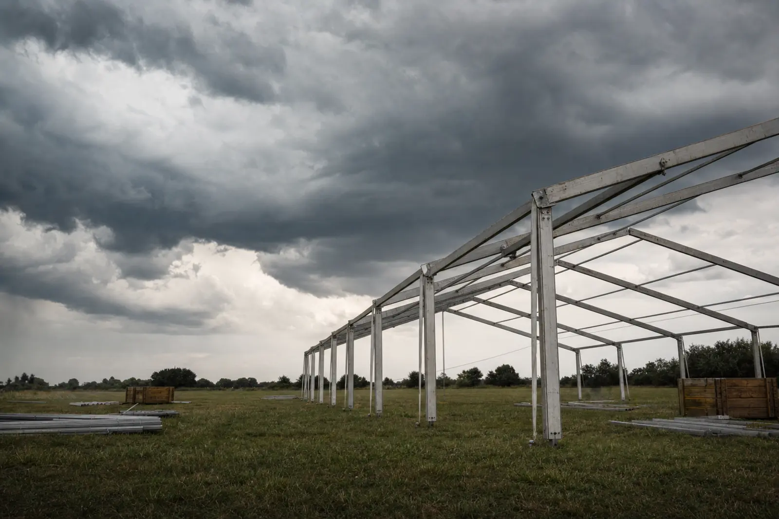 Dark storm clouds building over an open field where a marquee frame stands unfinished